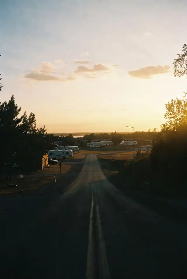 A two-lane road at dusk leading down toward an RV park, trailers visible in the evening light